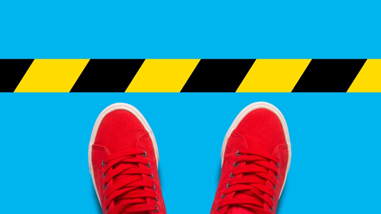 Female feet in red sneakers standing in front of a warning black-and-yellow line. Concept of the destruction of borders and violations of the rules. Flat lay, top view