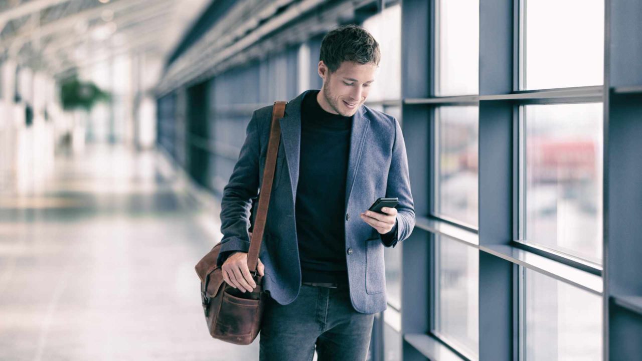 Mobile,Phone,Business,Man,Walking,In,Airport,With,Messenger,Bag